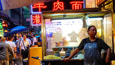 noodle vendor standing in front of cart of noodles and soup bowls