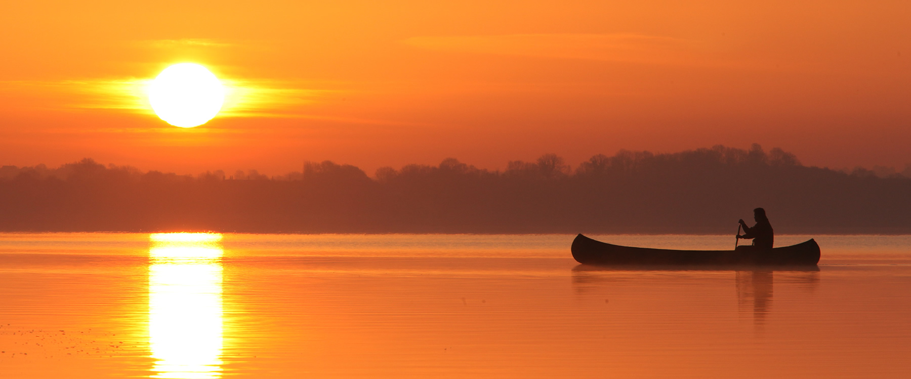 Person paddling in a canoe on a river at sunrise