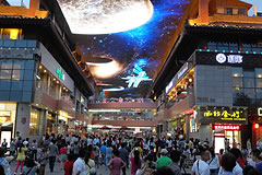 people walking in a mall with a giant LED screen overhead