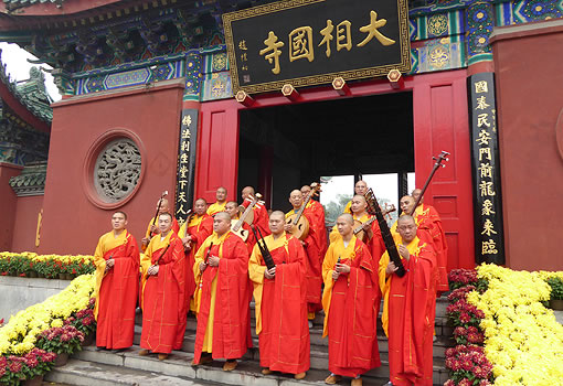 Group of Buddhist monks standing on temple steps, holding musical instruments