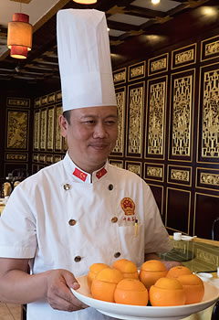 man in chef's uniform carrying a platter of cut oranges