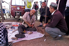 2 men crouching next to a man sitting on a blanket, working on leather belts